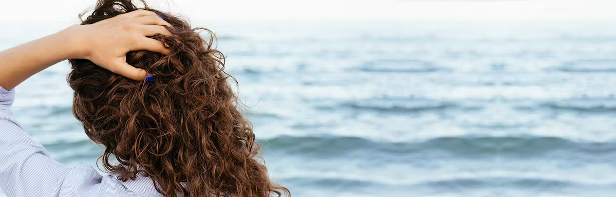 FFOR Hair banner image of back of woman holding hair in front of ocean 